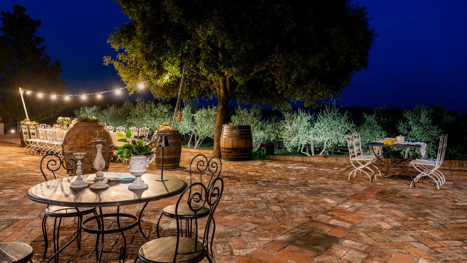 Un patio al aire libre con asientos de hierro forjado y luces colgantes por la noche.