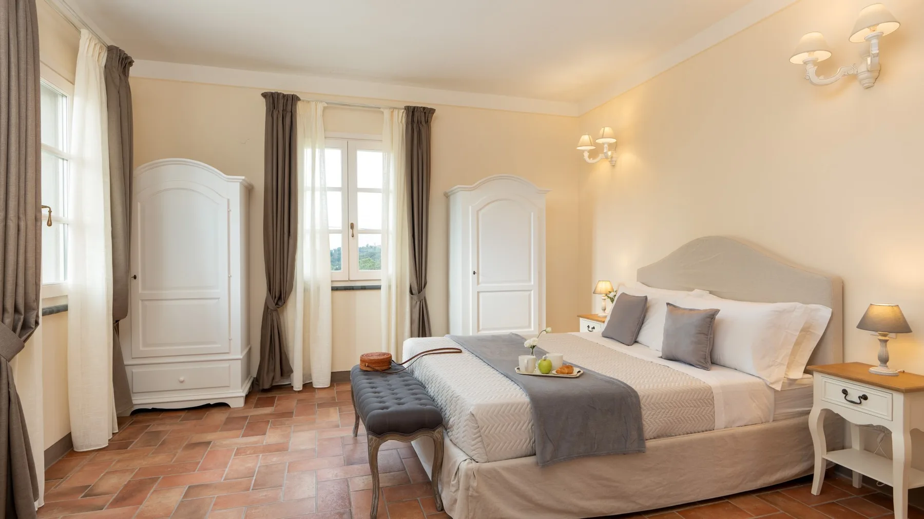 Un dormitorio luminoso con una cama, una mesita de noche y ventanas altas.