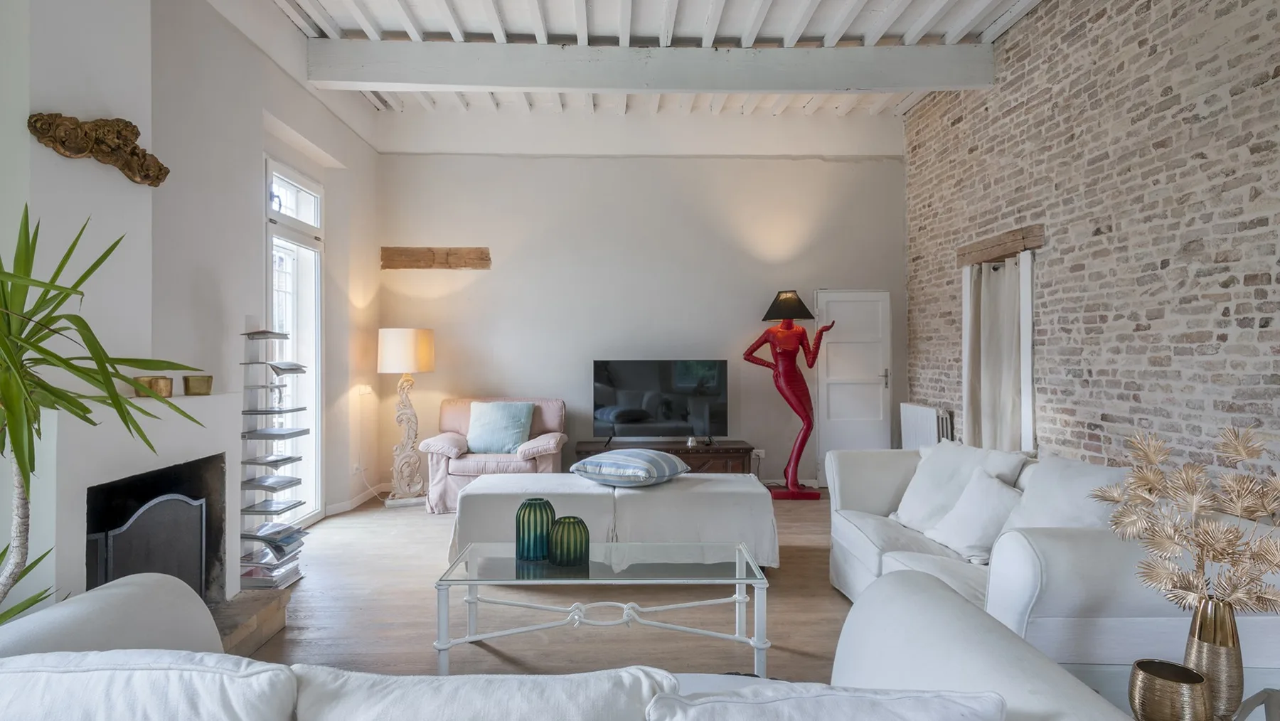 A bright living room with white seating, a television, and exposed ceiling beams.