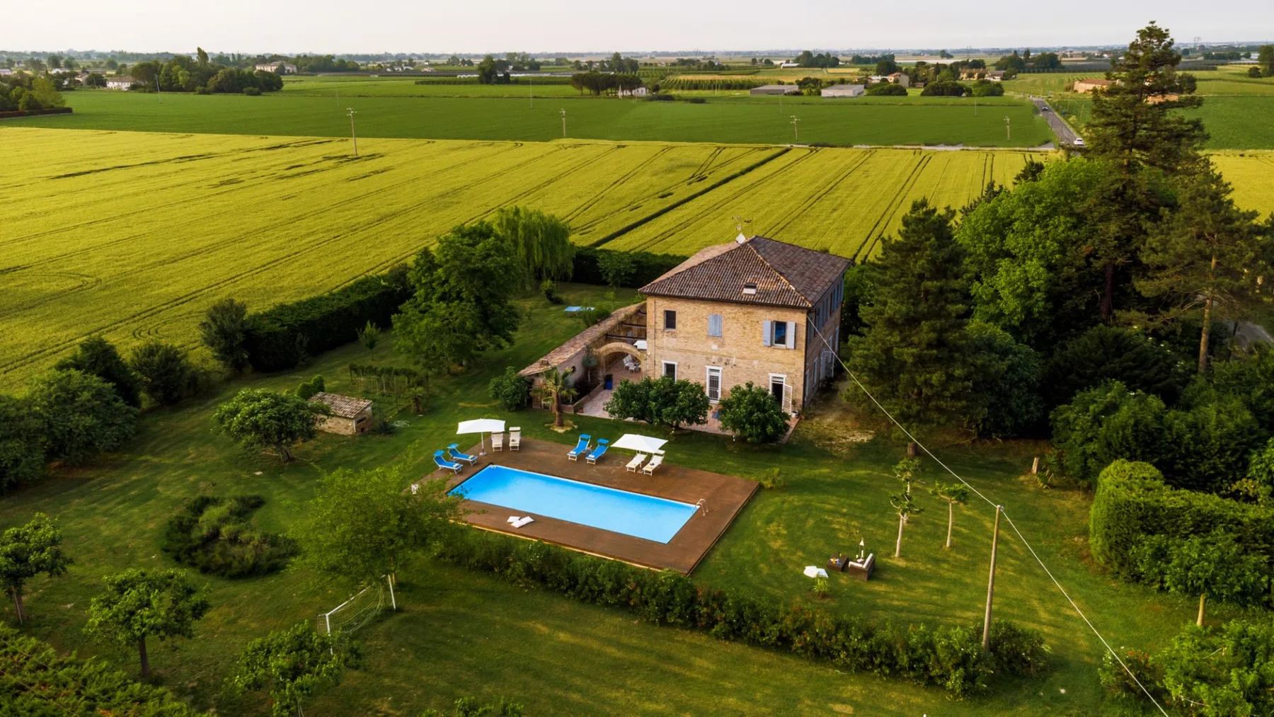 A countryside house and swimming pool sit beside expansive green fields.