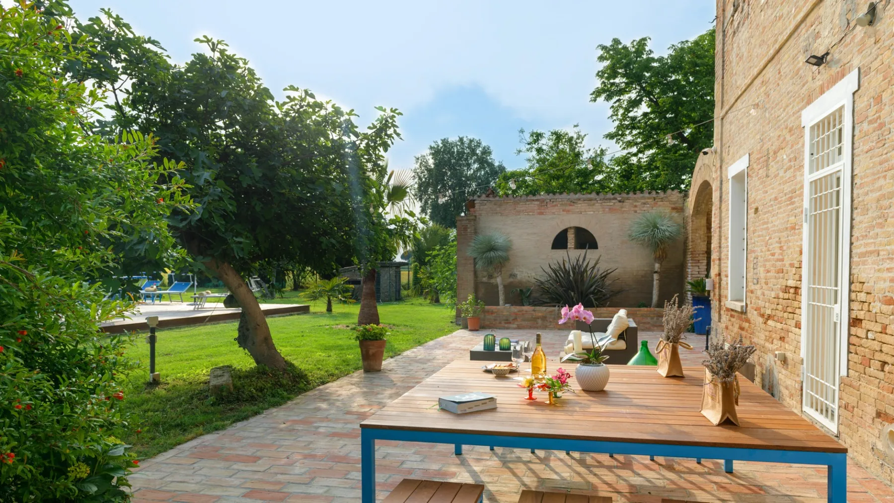 A garden patio with a wooden table set beside a brick building.