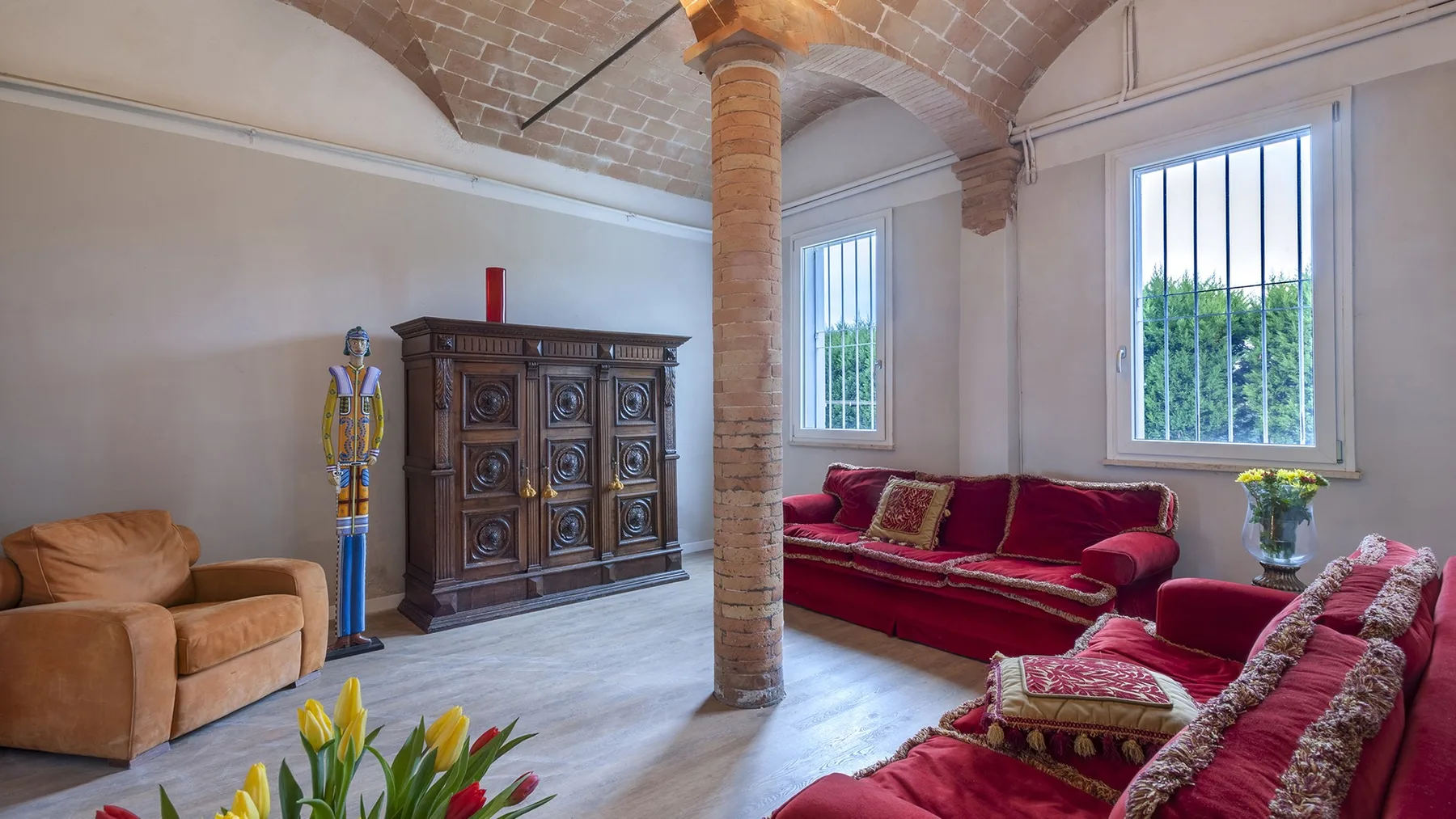 A living room with red seating, a wooden cabinet, and tall windows.