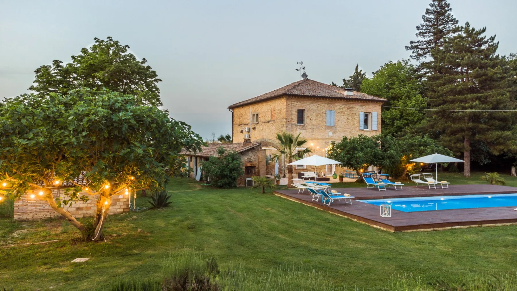 A landscaped outdoor pool area sits beside a two-story building and mature trees.