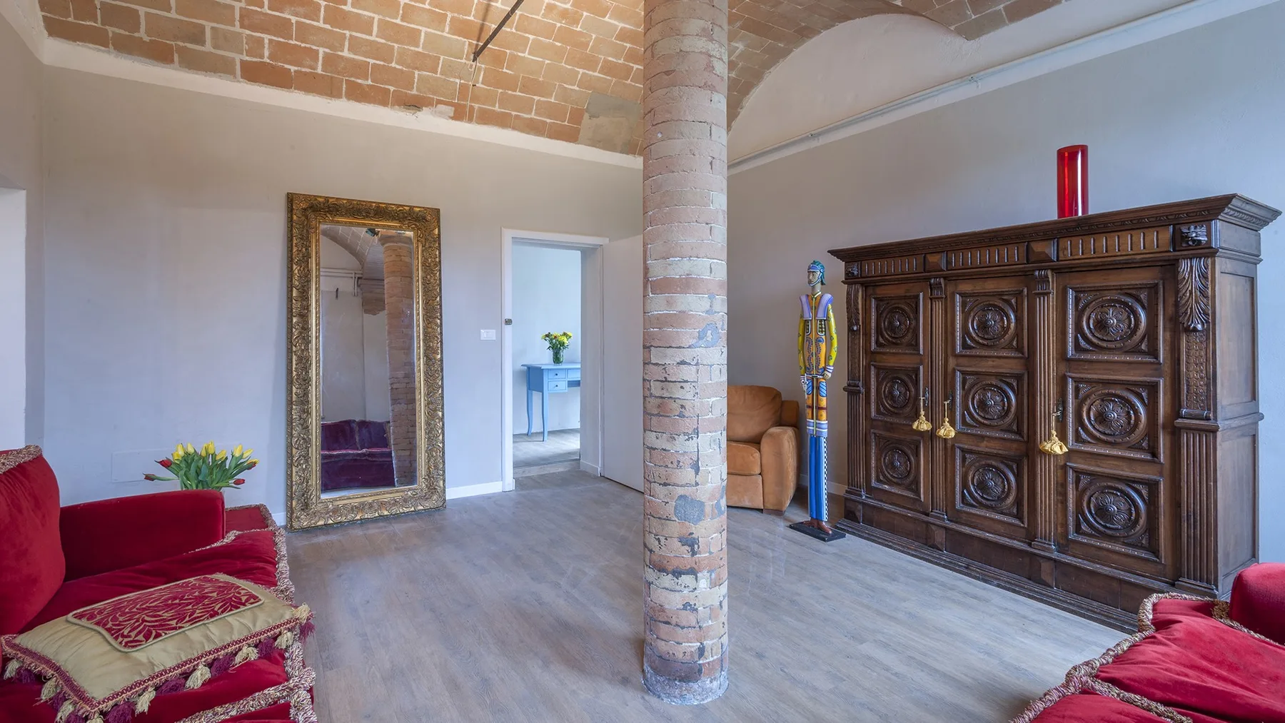 A living room with red seating, a carved wooden cabinet, and an exposed brick column.