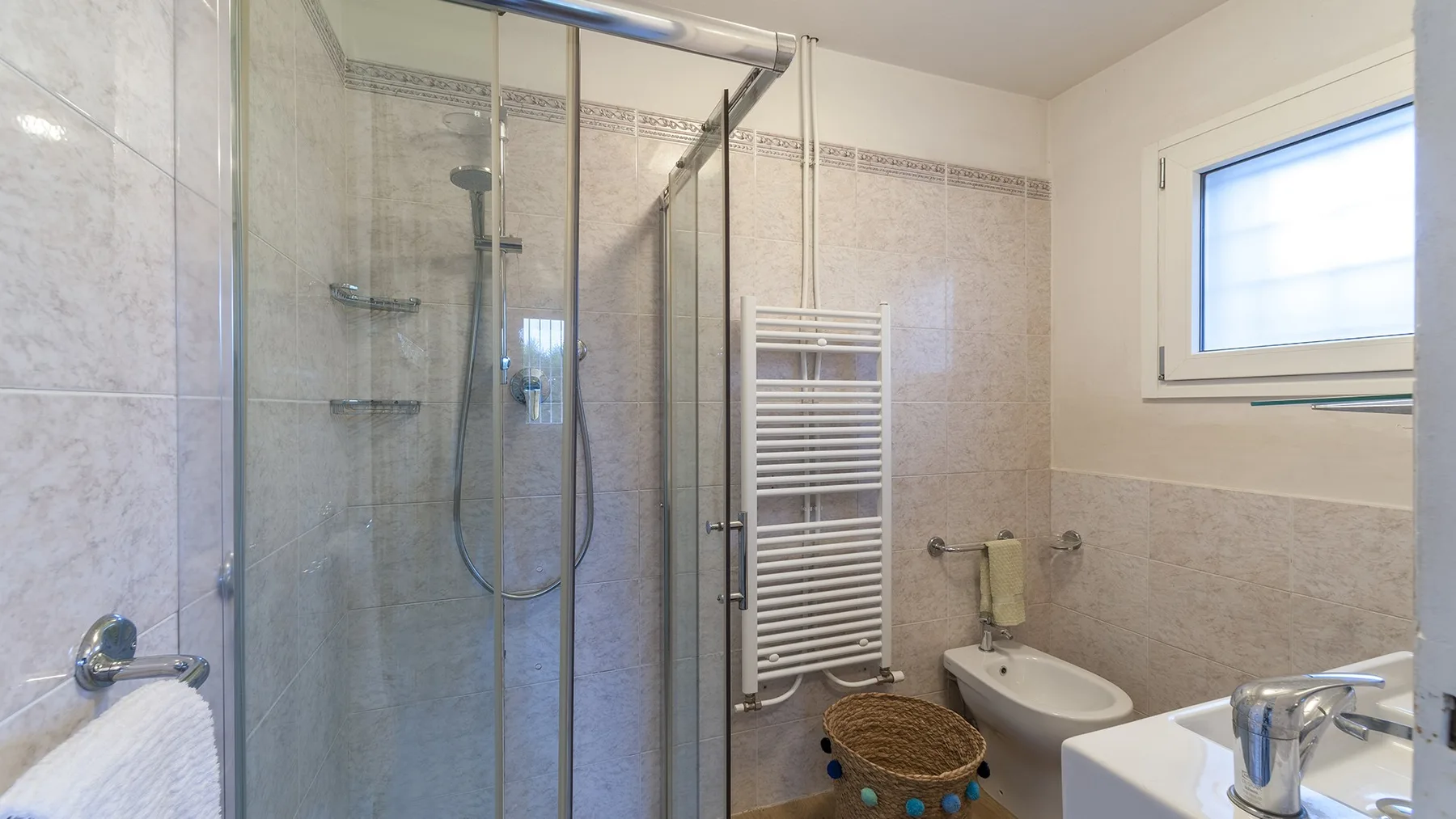A tiled bathroom with a glass shower, towel warmer, and sink.