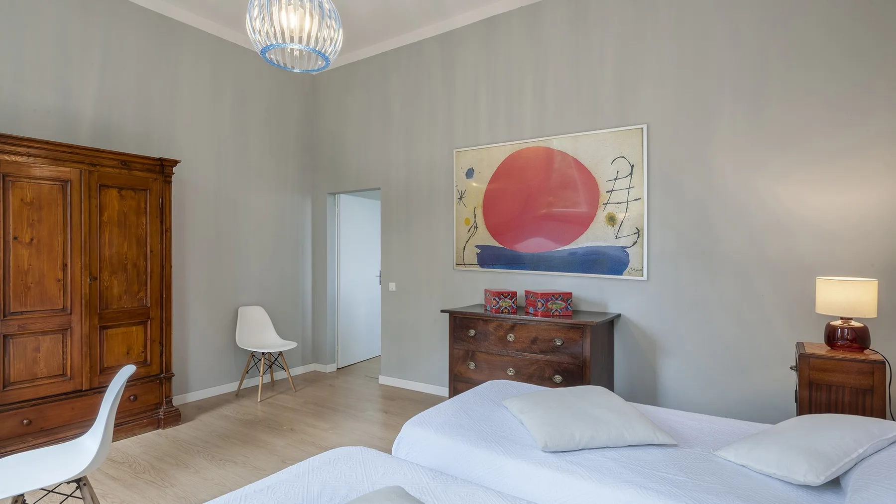 A bedroom with a bed, wooden dresser, and wall art.
