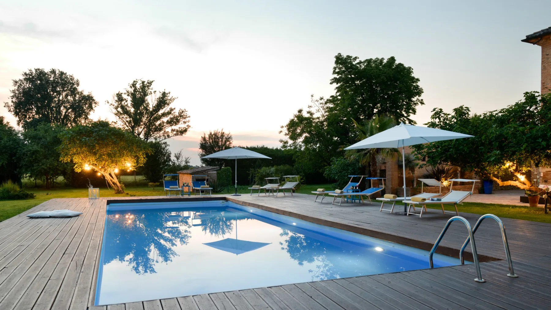 An outdoor swimming pool is surrounded by a wooden deck, loungers, and umbrellas.