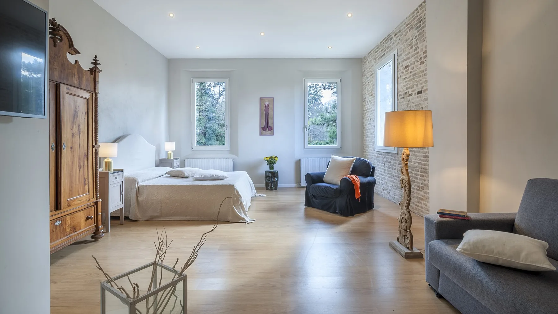 A bright bedroom with a bed, seating, and tall windows.