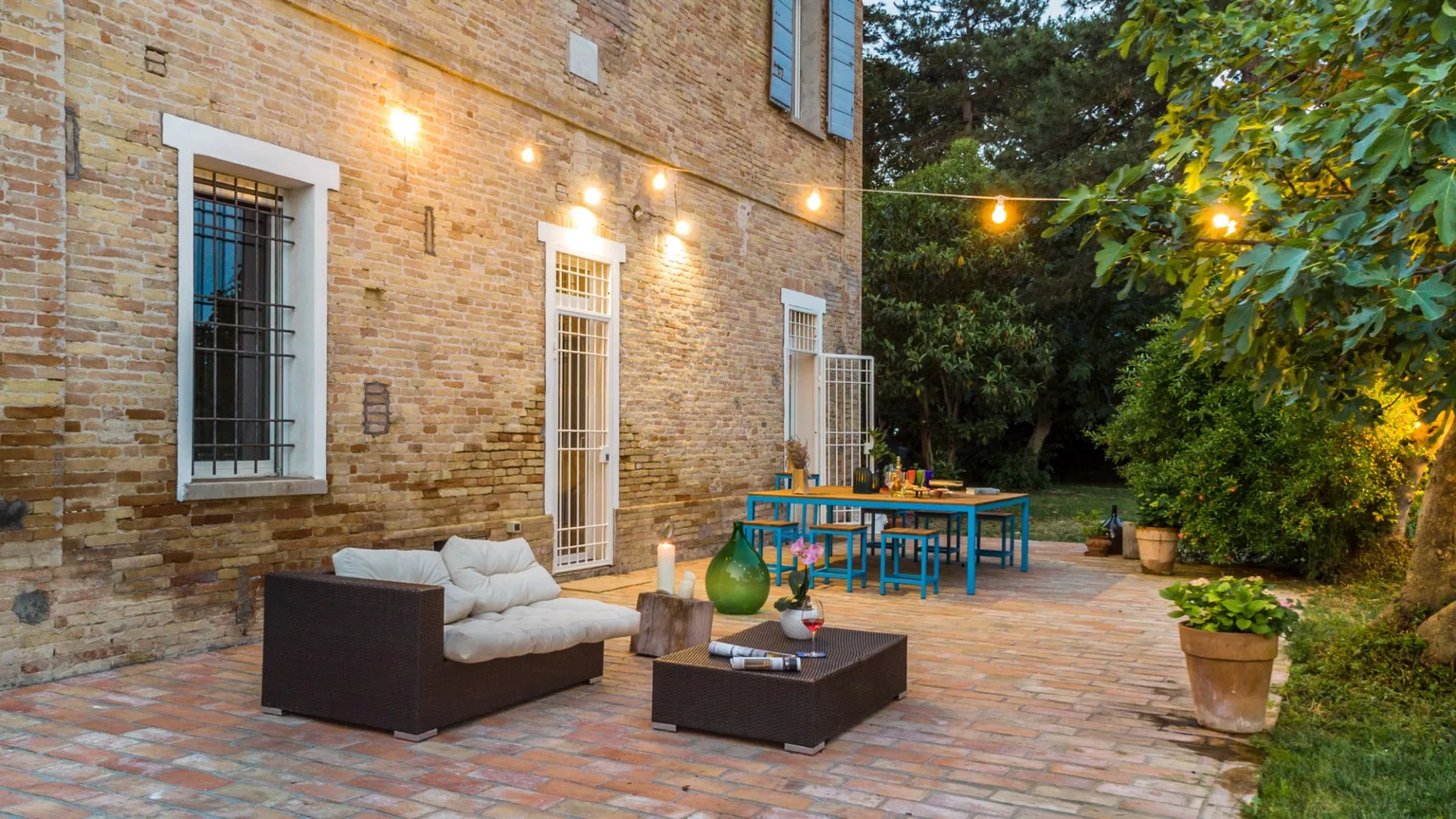 A brick patio with outdoor seating, a table, and string lights.