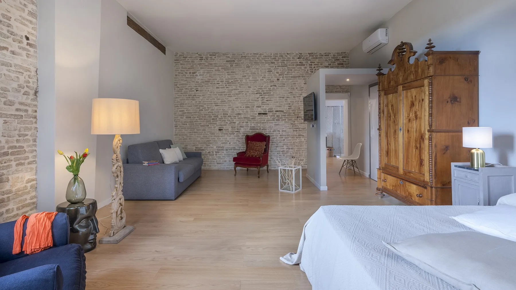 A bedroom with a bed, seating, and a large wooden wardrobe.