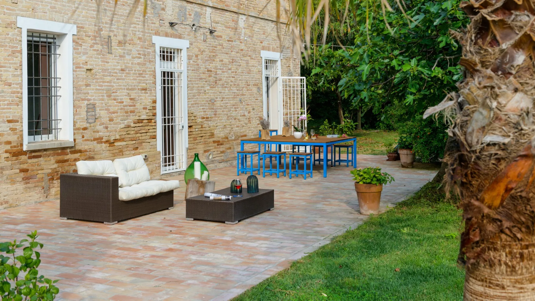 A brick patio with outdoor seating and a table beside a grassy garden.