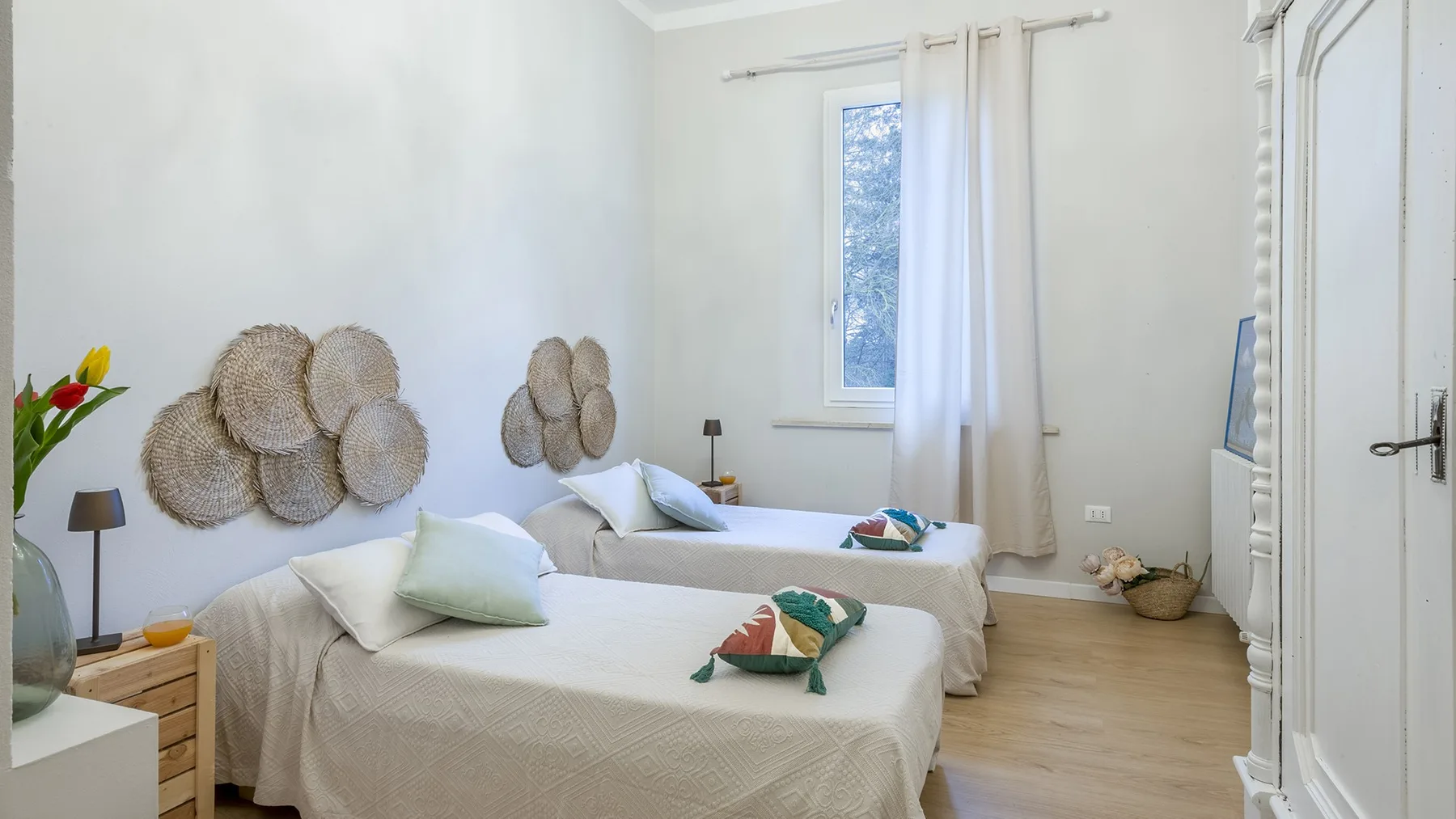 A bright bedroom with two beds, light bedding, and a window with curtains.