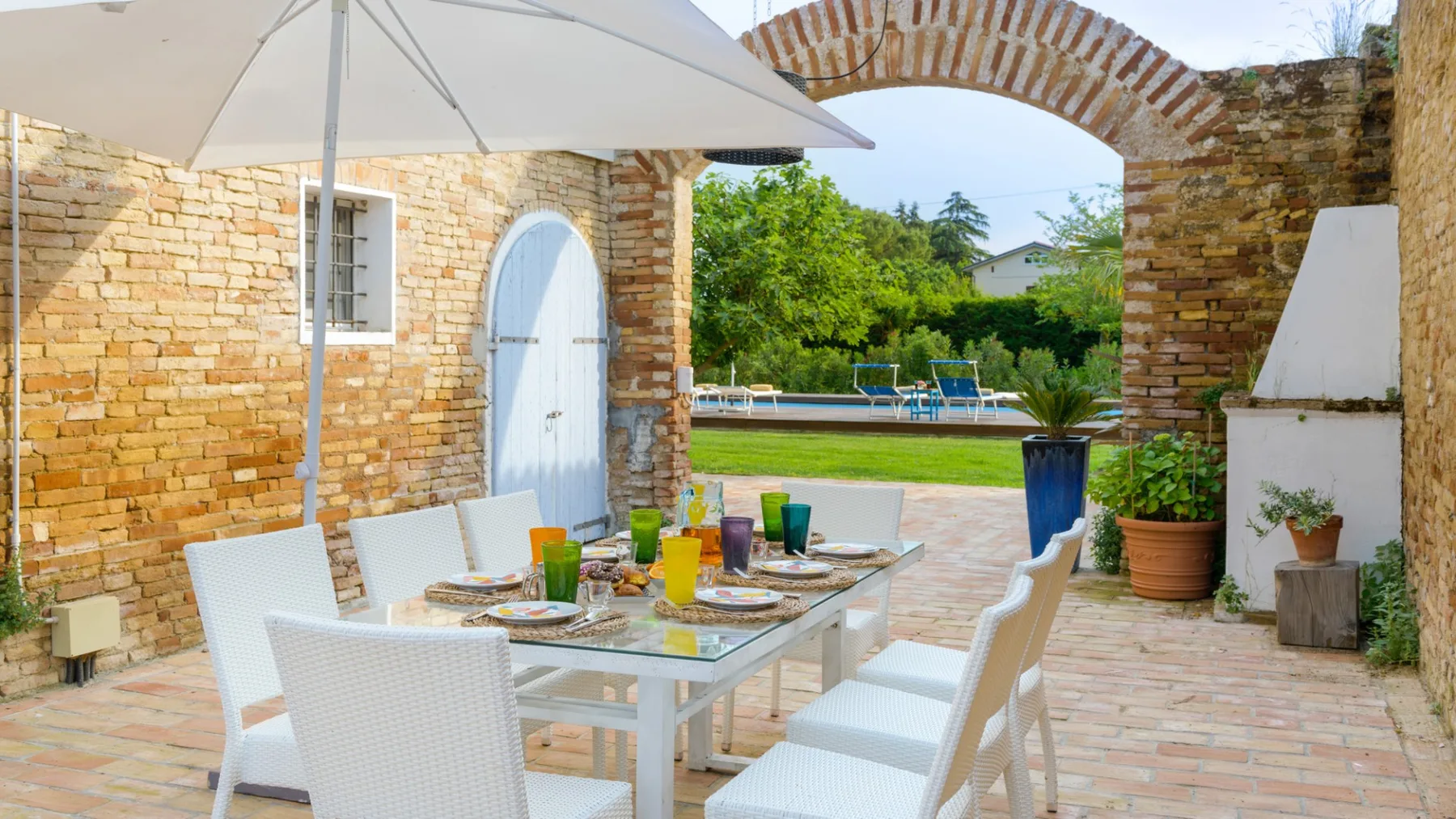 An outdoor dining area sits beneath a brick arch, with a pool visible beyond.