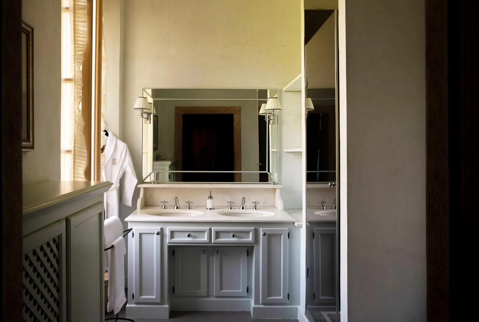 A bathroom vanity with a wide mirror and a white robe hanging nearby.
