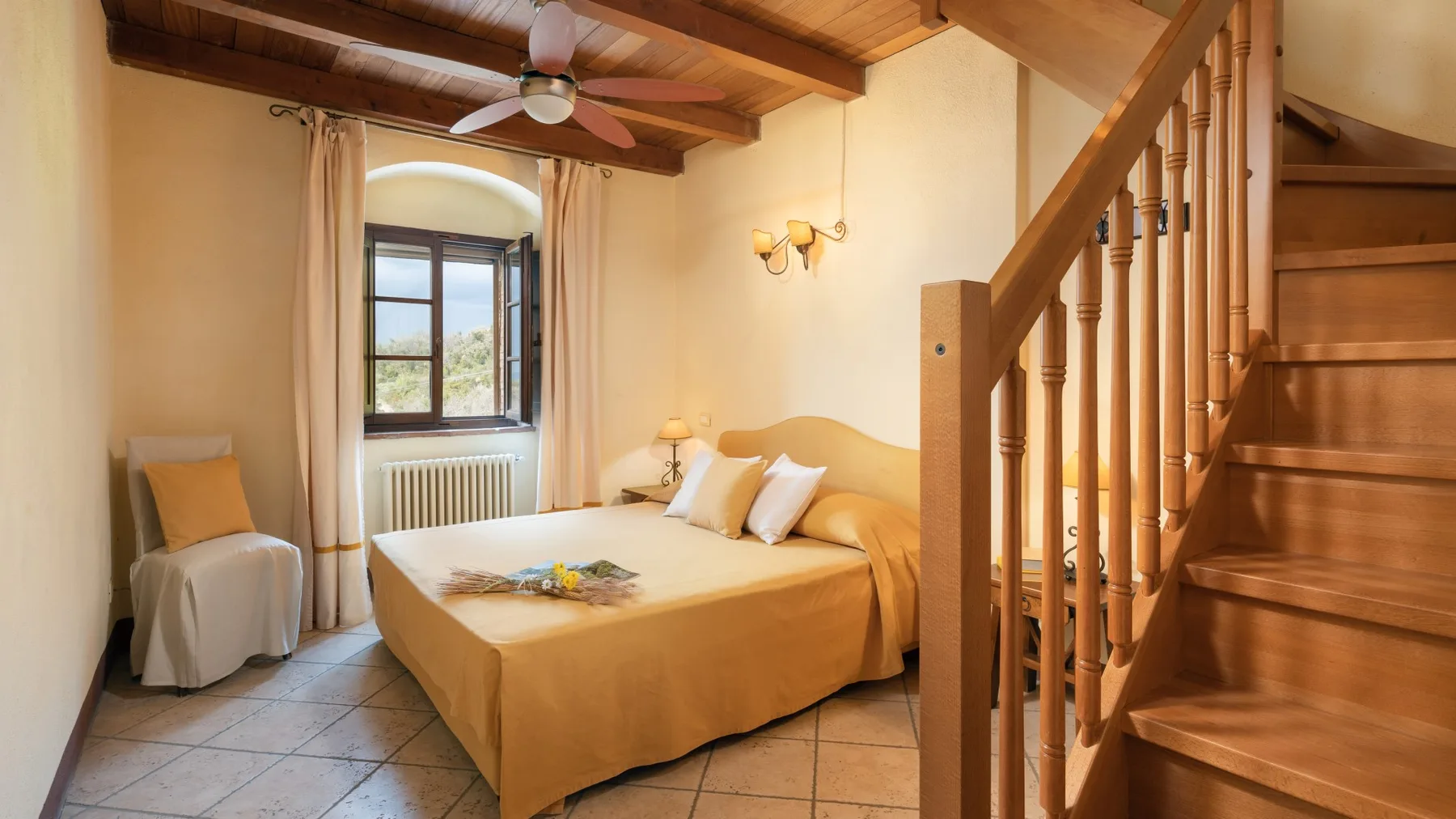Dormitorio con una cama doble, una ventana y una escalera de madera.