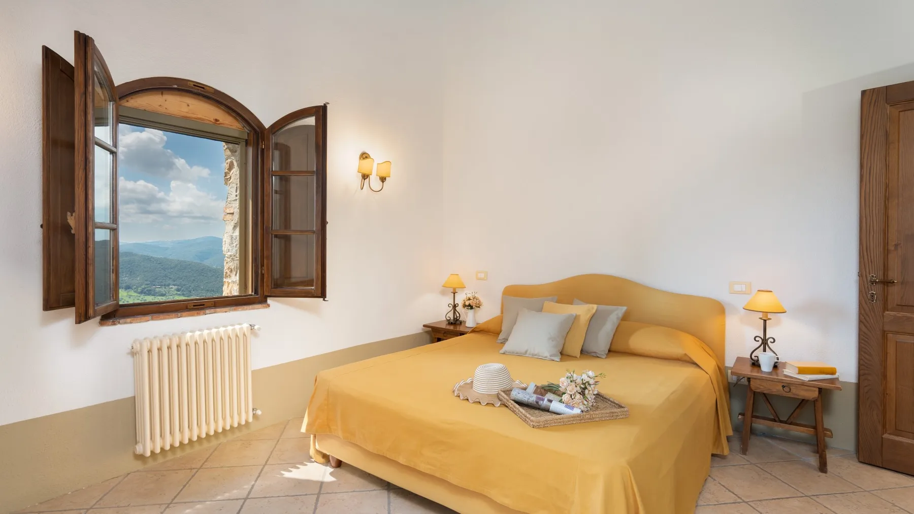 Un dormitorio con una cama amarilla y una ventana abierta con vistas a las colinas.