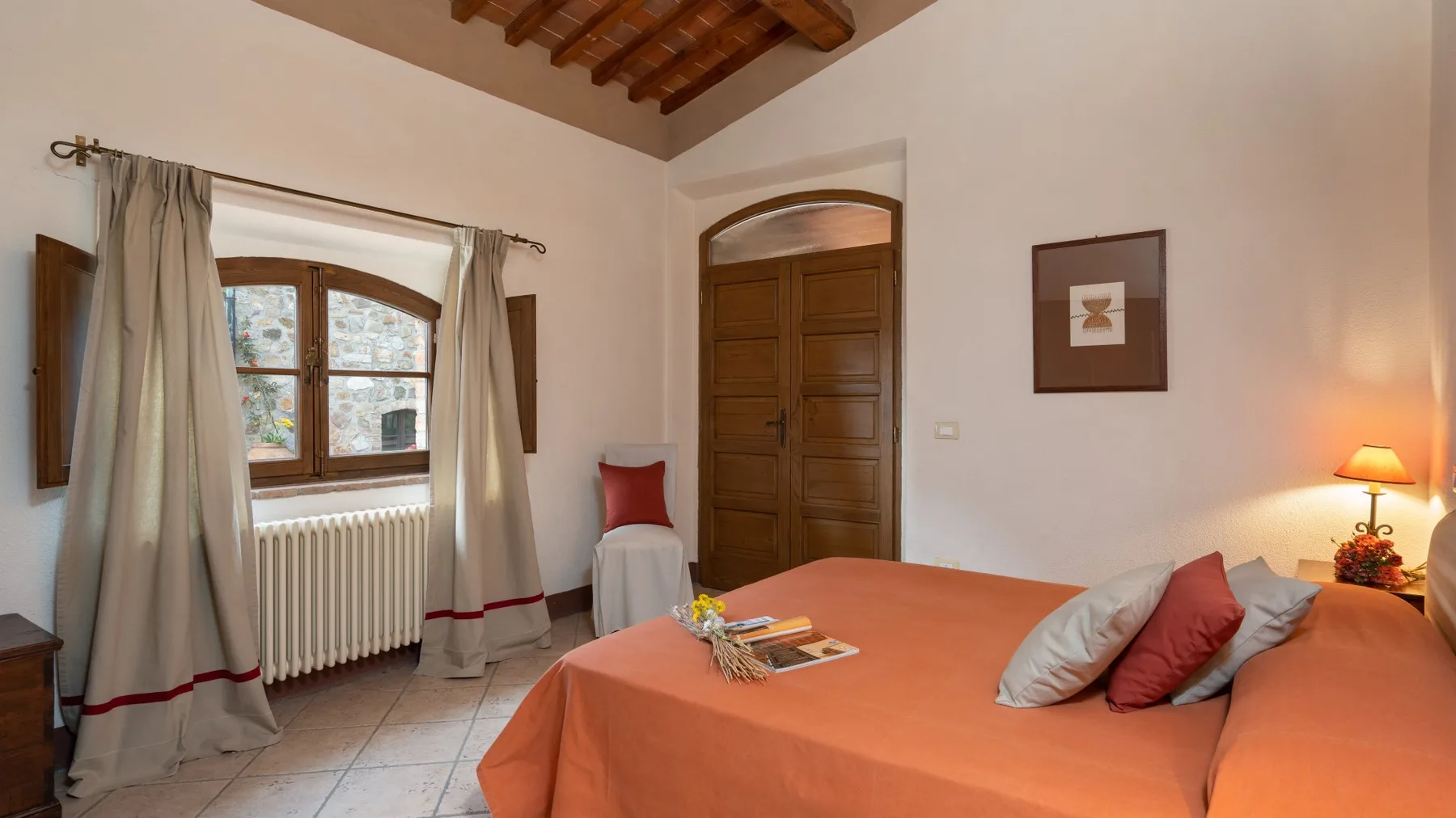 Un dormitorio con una colcha naranja, una puerta de madera y una ventana con cortinas.