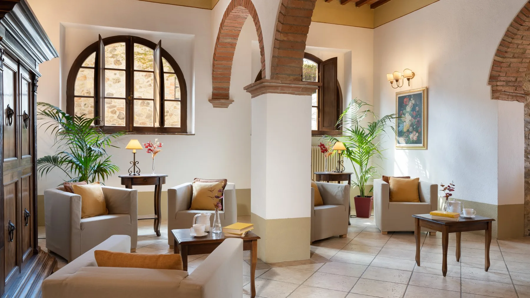 Una sala de estar con asientos, plantas en macetas y ventanas arqueadas.