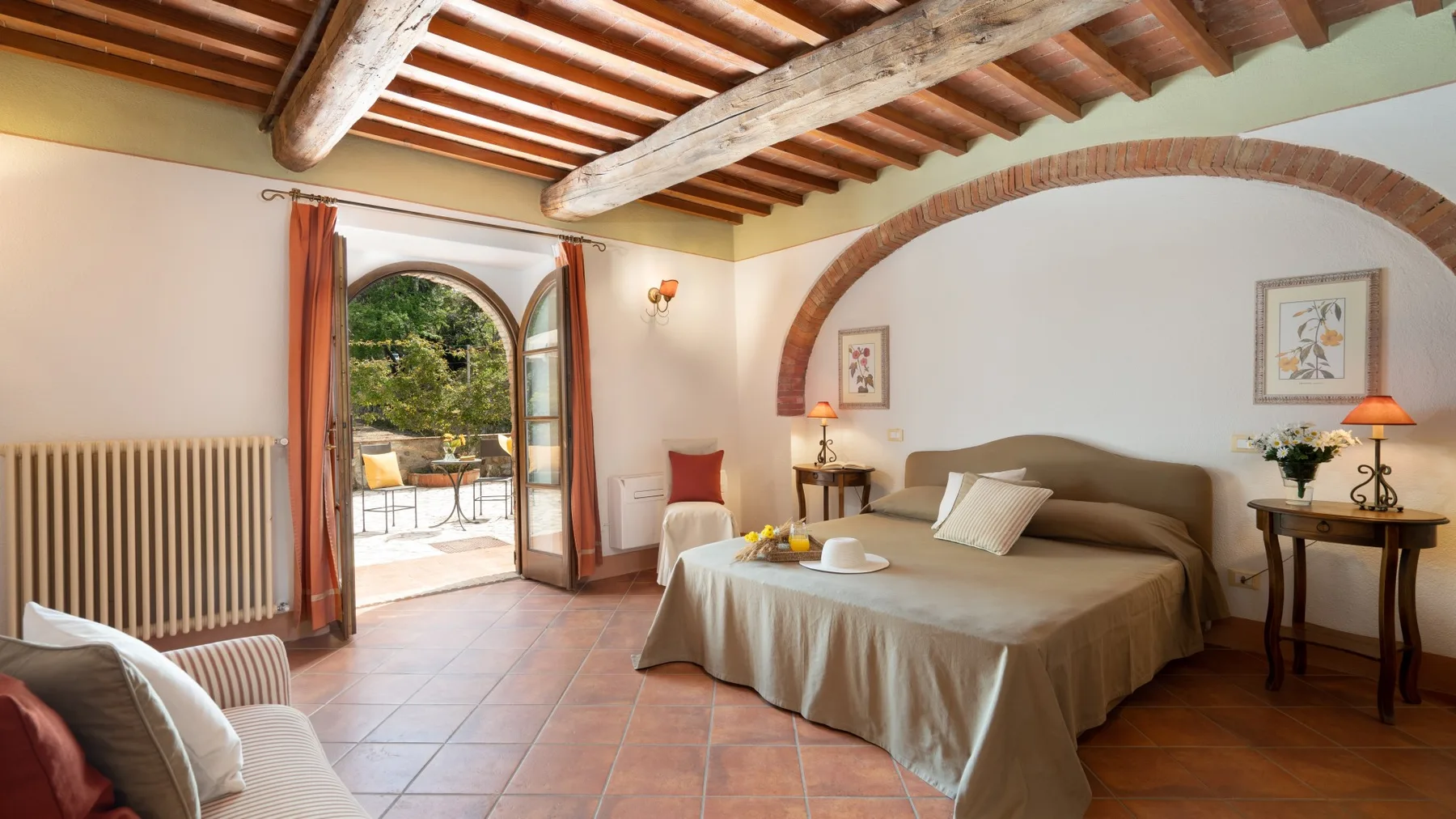 Un dormitorio con una cama grande, vigas de madera a la vista y una puerta arqueada que da a un patio.