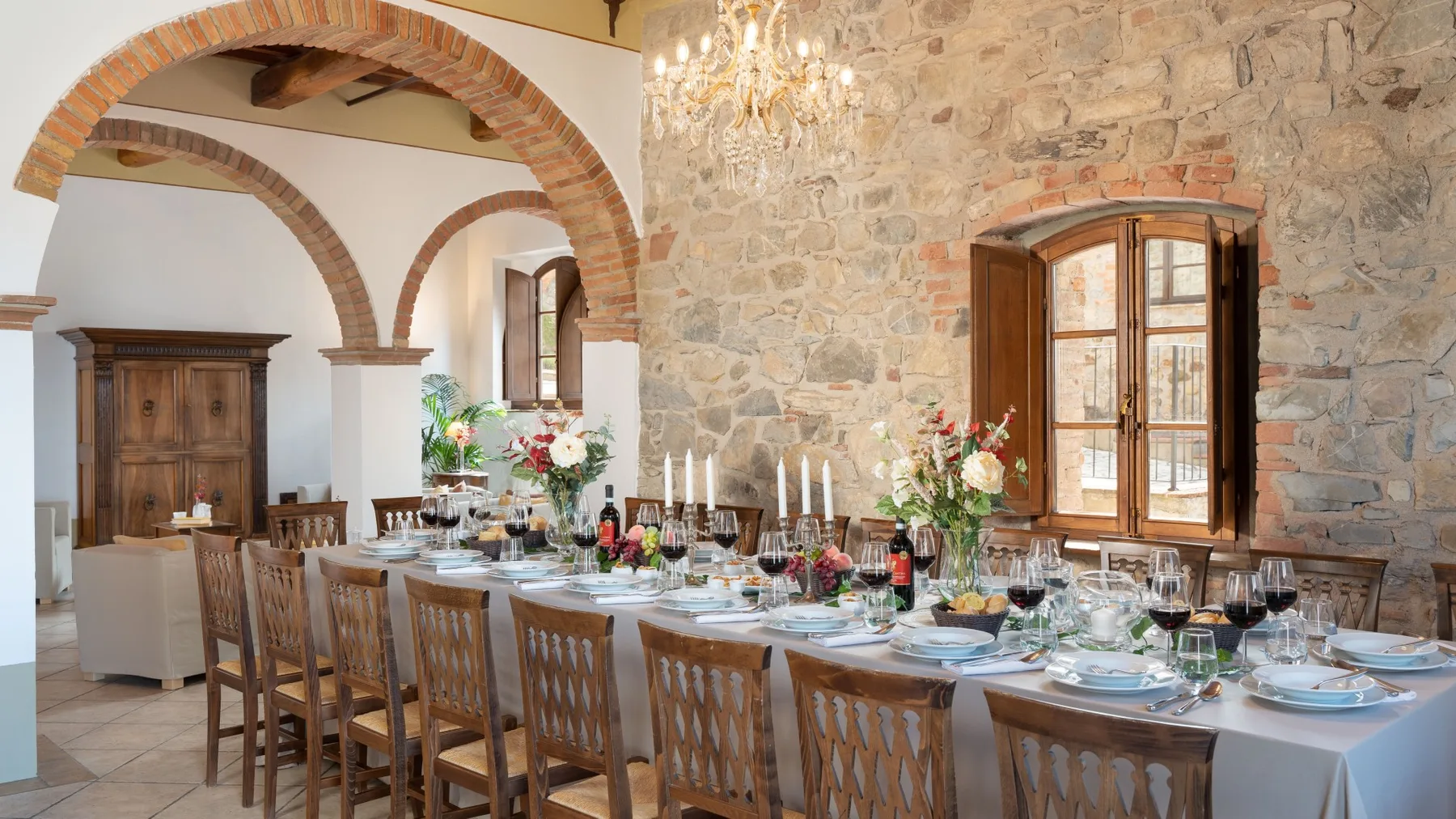 Un comedor con una mesa larga preparada para comer, bajo paredes de piedra y arcos de ladrillo.