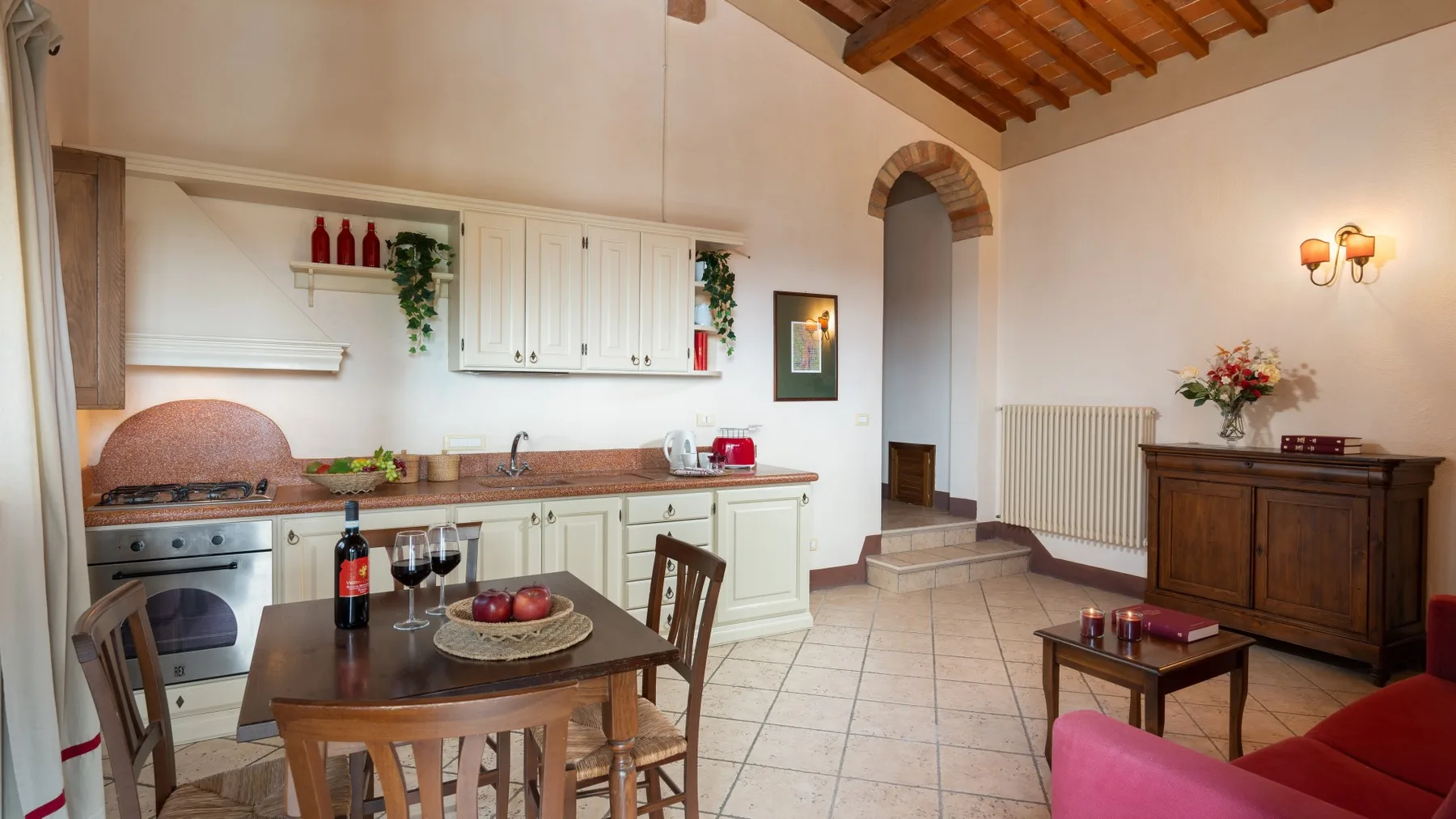 Comedor con una mesa de madera y armarios blancos de cocina bajo un techo con vigas.