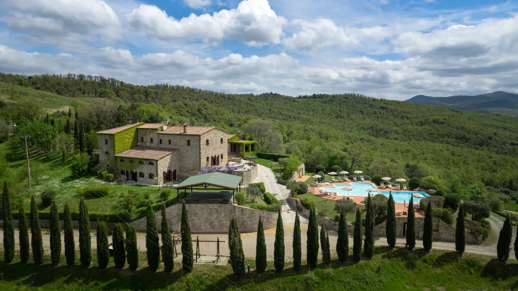 Una finca rural con piscina, rodeada de colinas boscosas y cipreses.