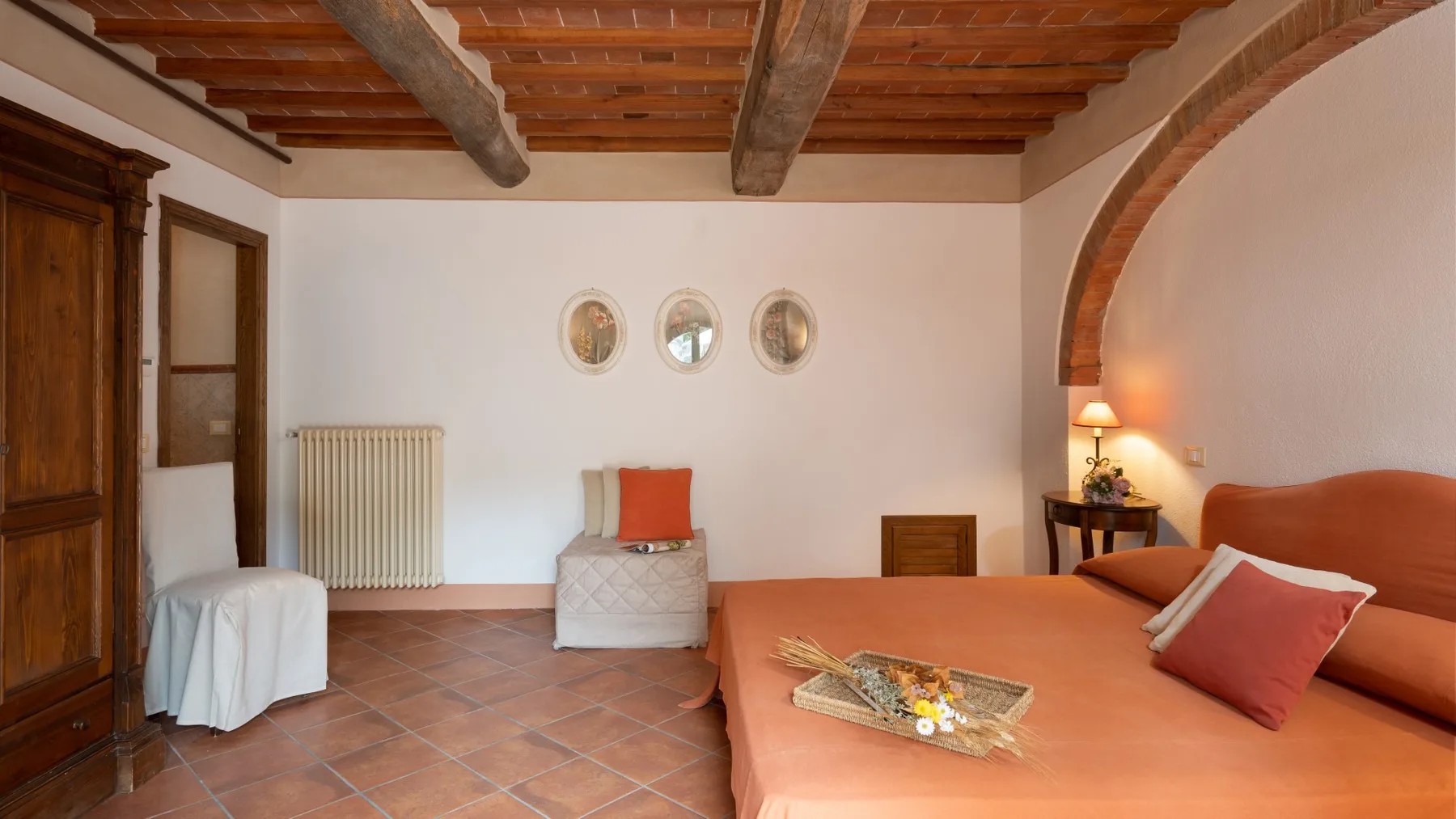 Un dormitorio con una cama color terracota, vigas de madera vistas y una pequeña zona de descanso.