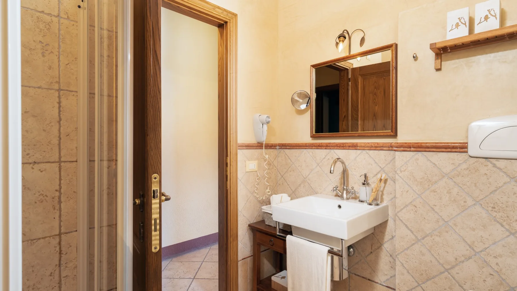 Un baño con lavabo blanco, espejo y paredes de azulejos.