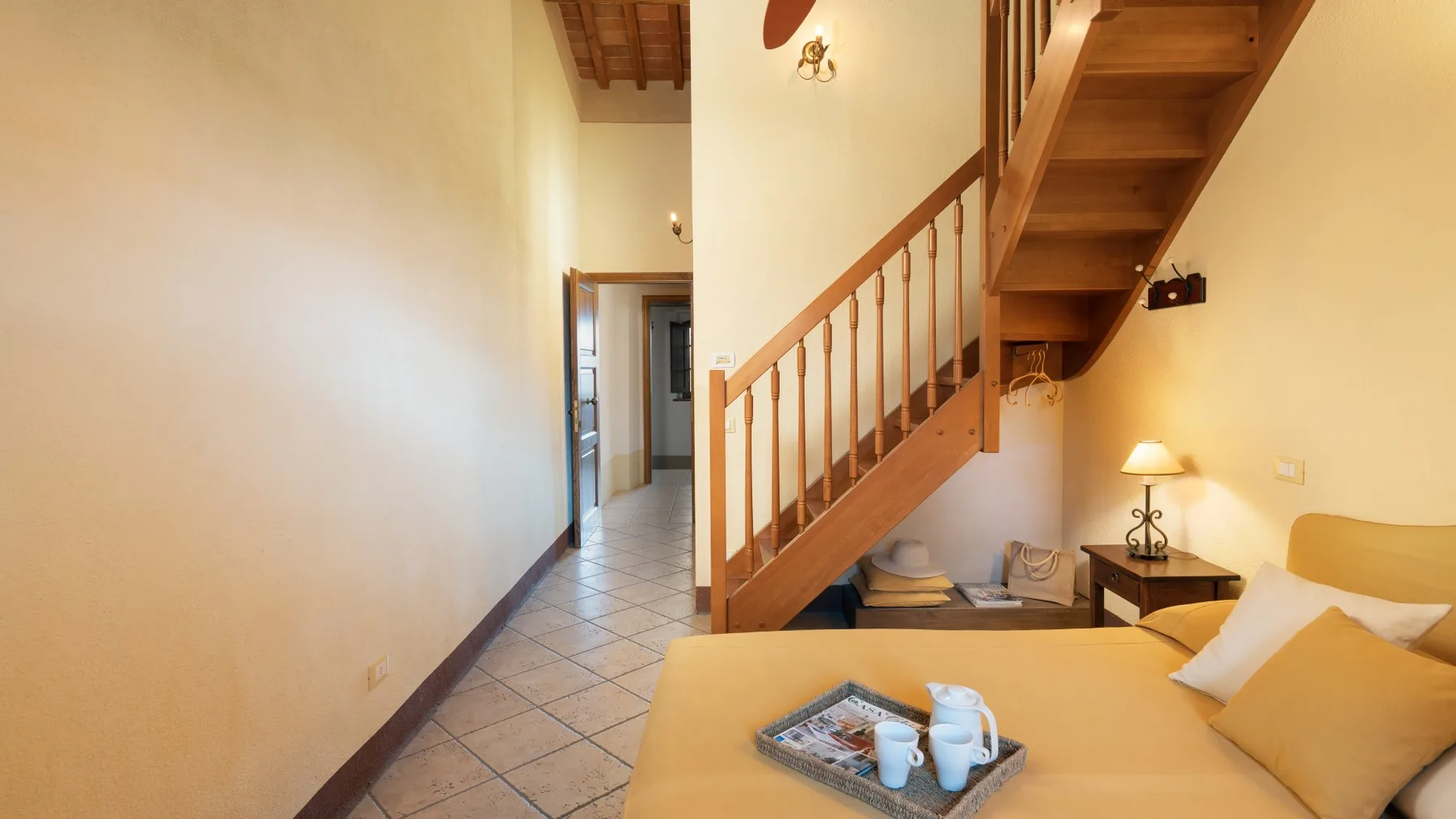 Un pasillo de baldosas se abre a una zona de estar bajo una escalera de madera.