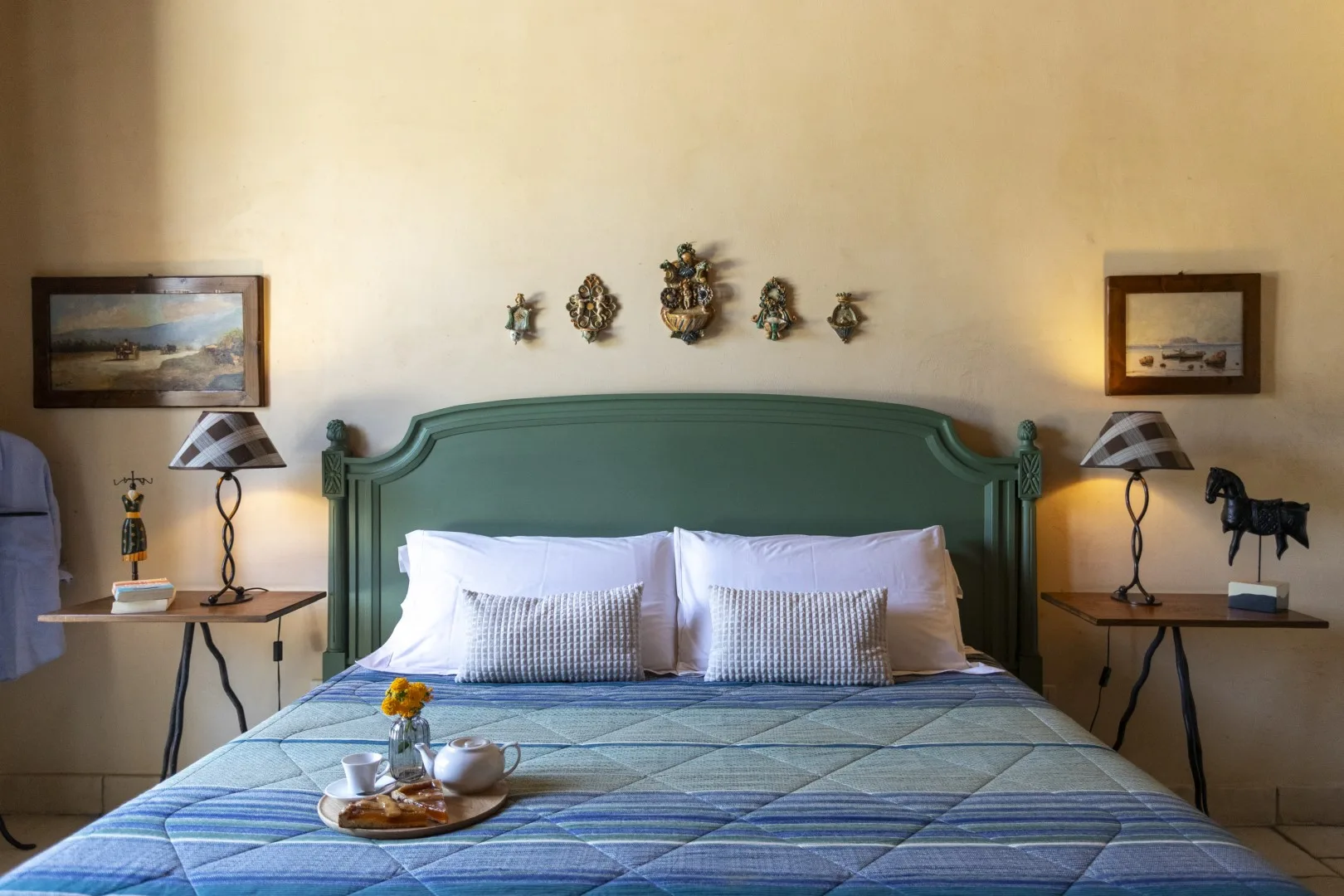 Un dormitorio con cabecero verde, ropa de cama azul y mesas auxiliares a juego.