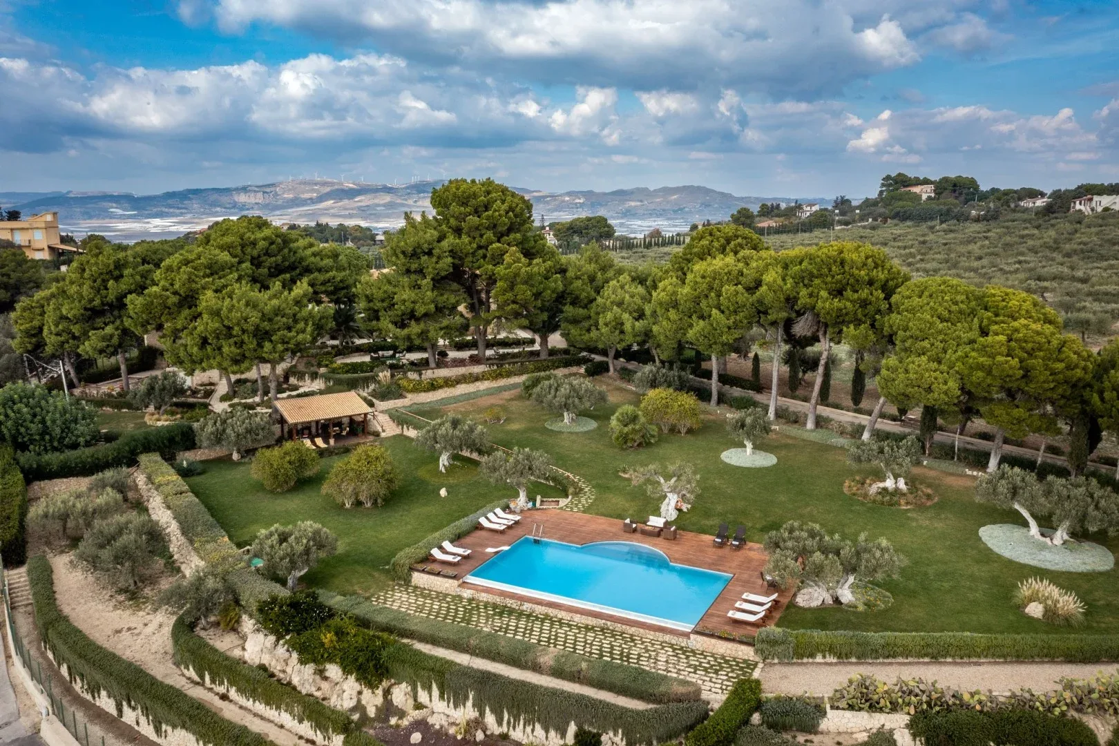 Una piscina al aire libre se encuentra en un jardín ajardinado bajo una ladera arbolada.