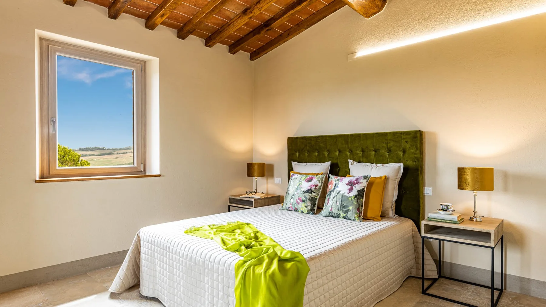 A bedroom with a double bed, green headboard, and window overlooking the landscape.