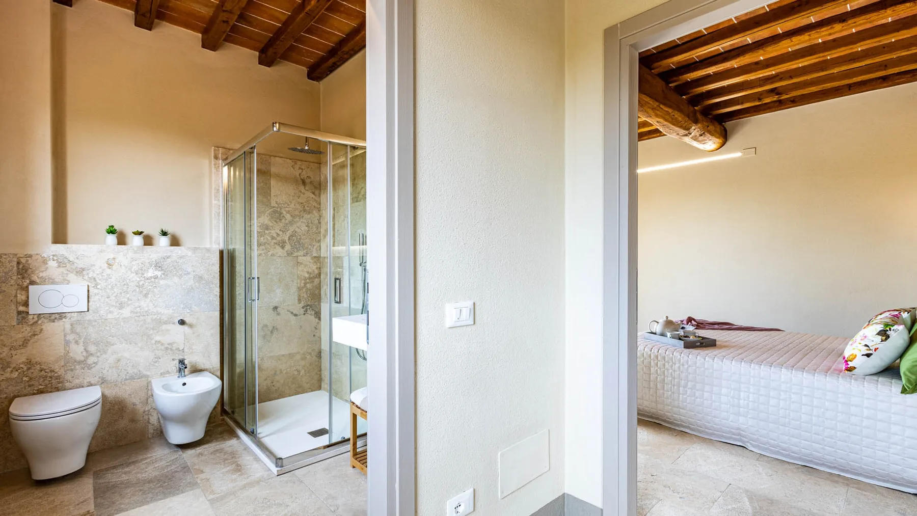 A bathroom with a glass shower and stone-patterned walls beside a bedroom.