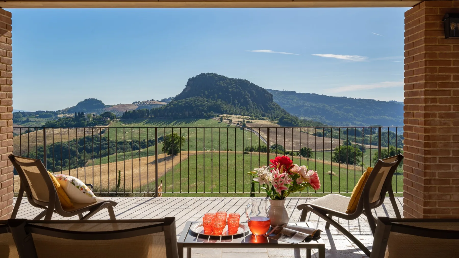 A covered outdoor seating area overlooks green hills and a mountain.