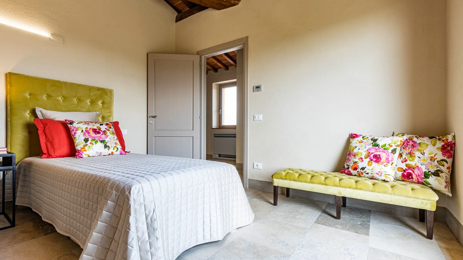 A bedroom with a bed and a cushioned bench beside the doorway.