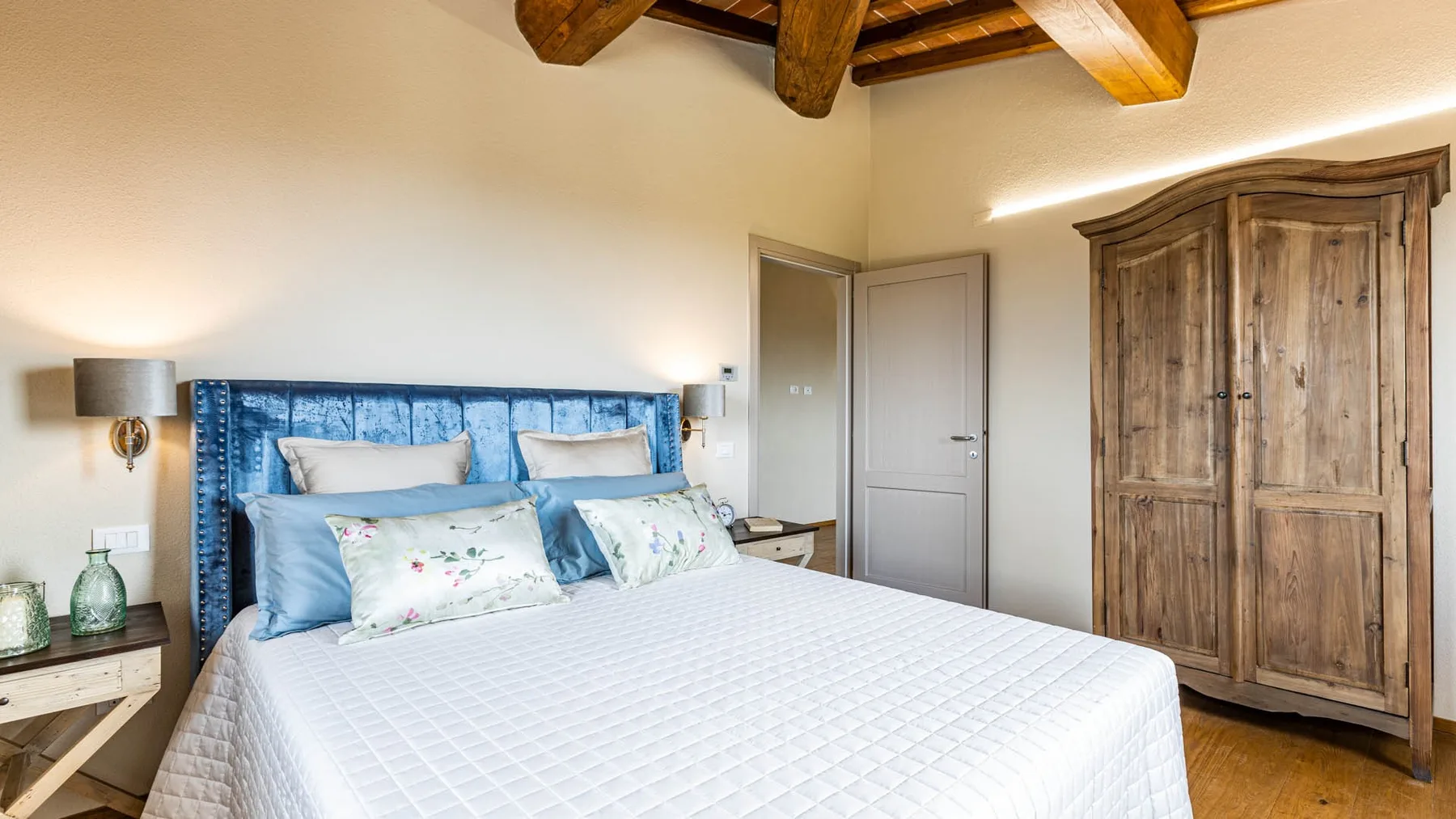 A bedroom with a large bed, blue headboard, and wooden wardrobe.
