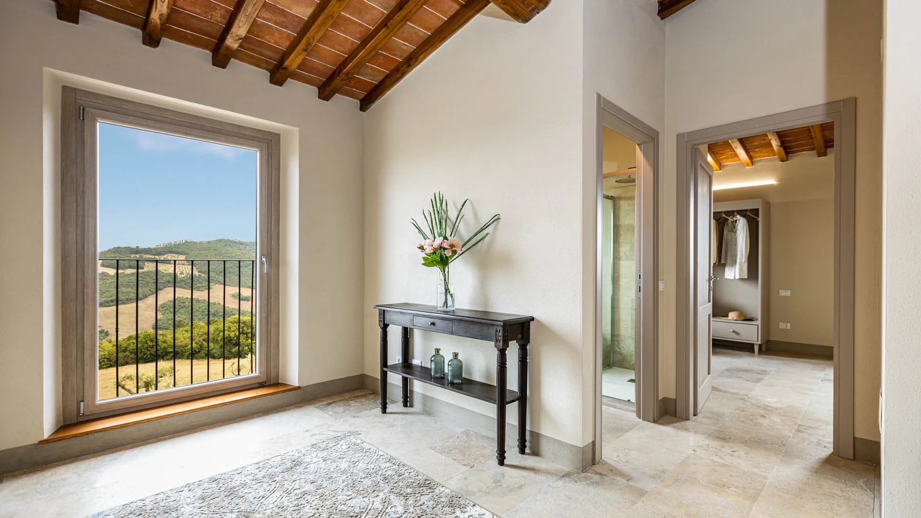 A bright bedroom with an exposed wooden ceiling and a window overlooking green hills.