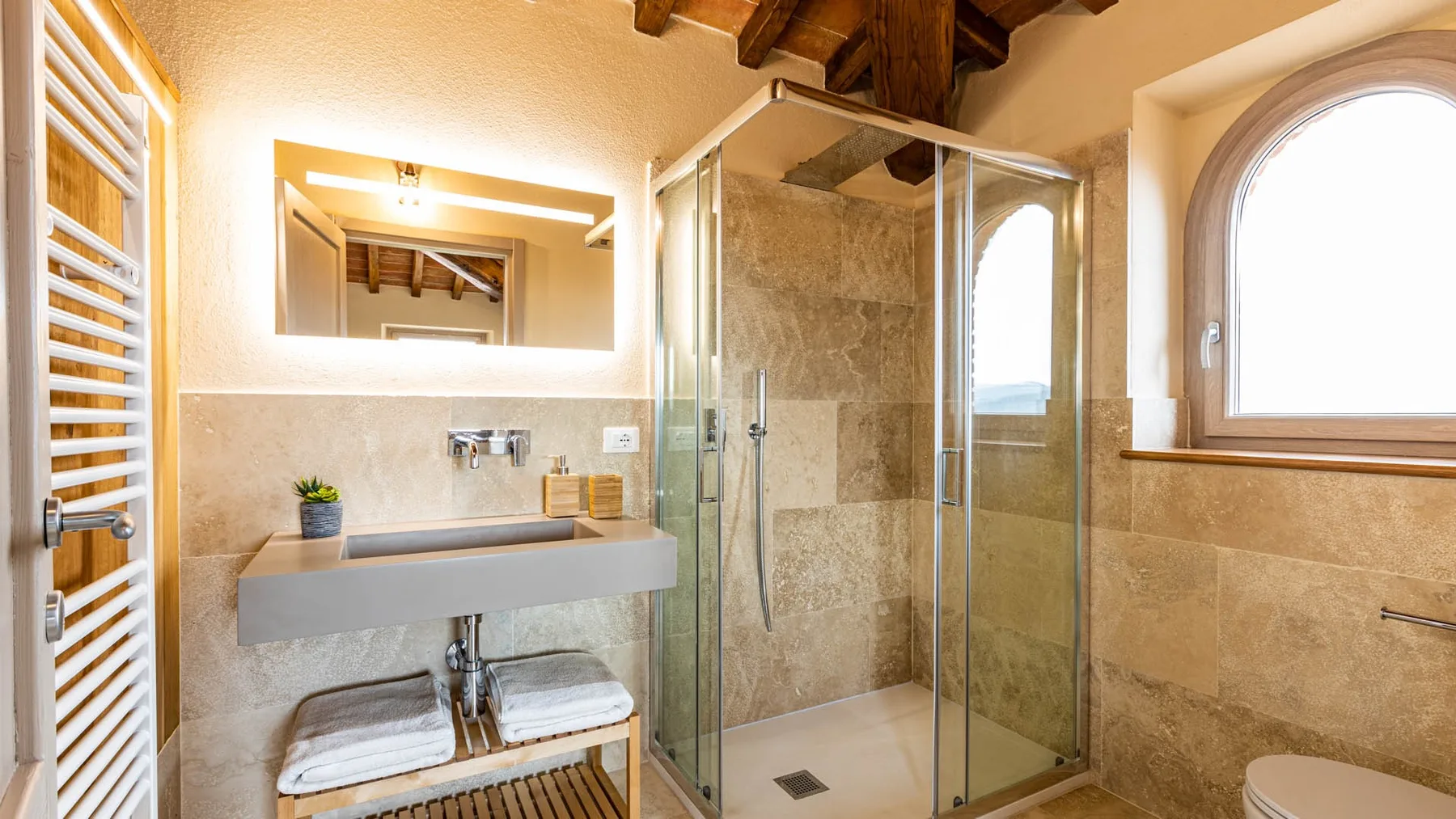 A bathroom with a glass shower, sink, and arched window.
