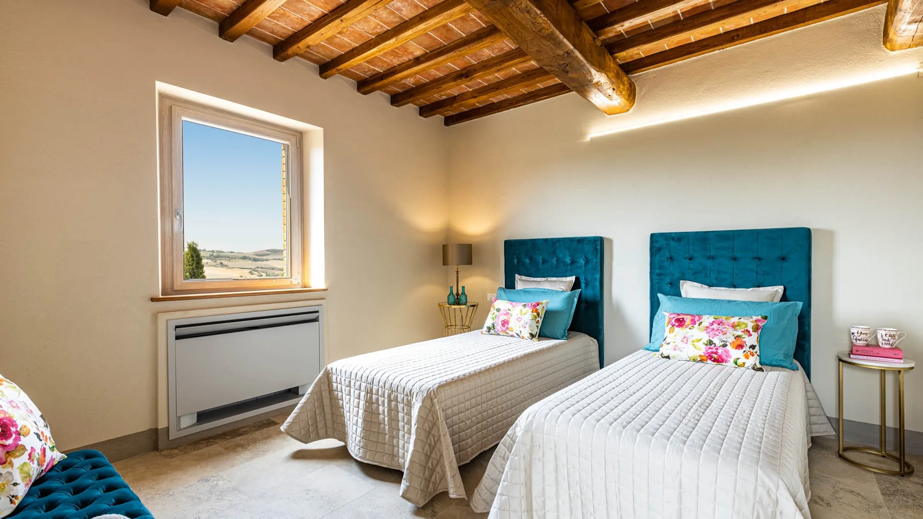 A bedroom with two beds, teal headboards, and a window overlooking the landscape.