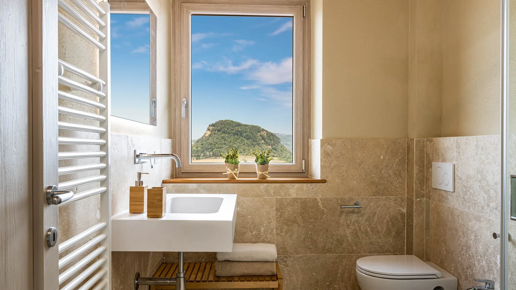 A bathroom with a sink and window overlooking a green hill.