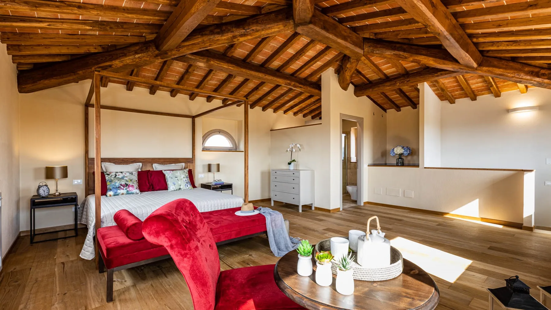 A bedroom with a red bed beneath a timber-beamed ceiling.
