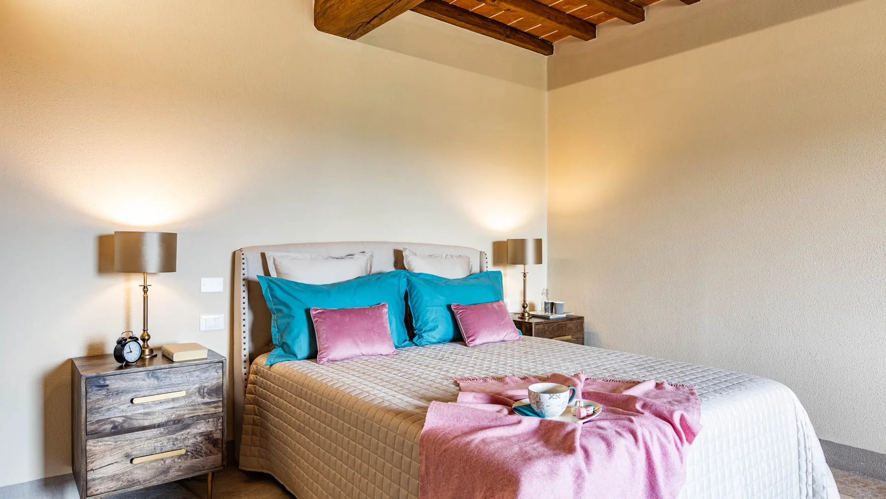 A bedroom with a neatly made bed, colorful pillows, and matching bedside tables.