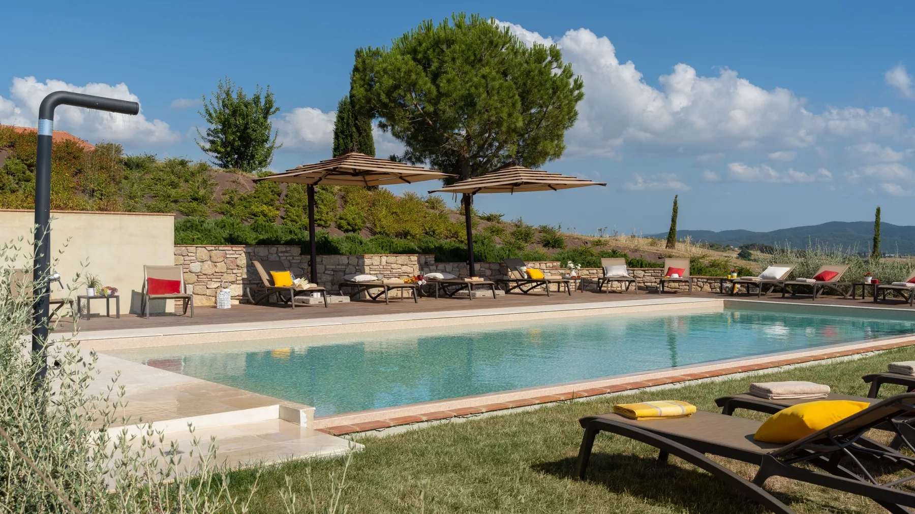 An outdoor swimming pool beside a sunlit terrace with loungers and umbrellas.