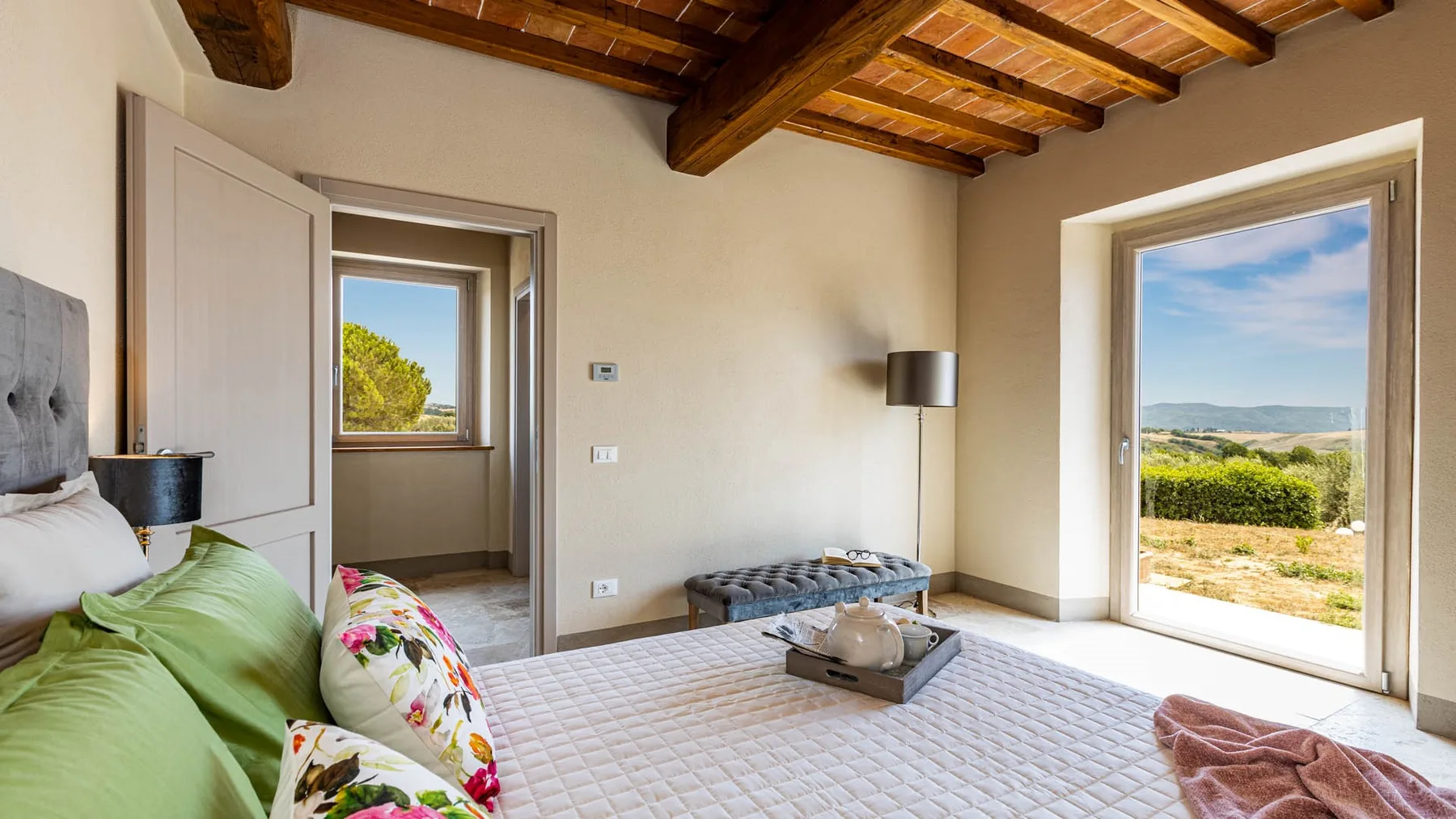 A bedroom with a bed, a small bench, and a large window overlooking greenery.