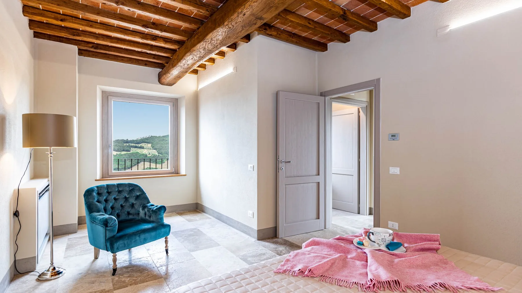 A bright bedroom with a teal armchair beside a large window.