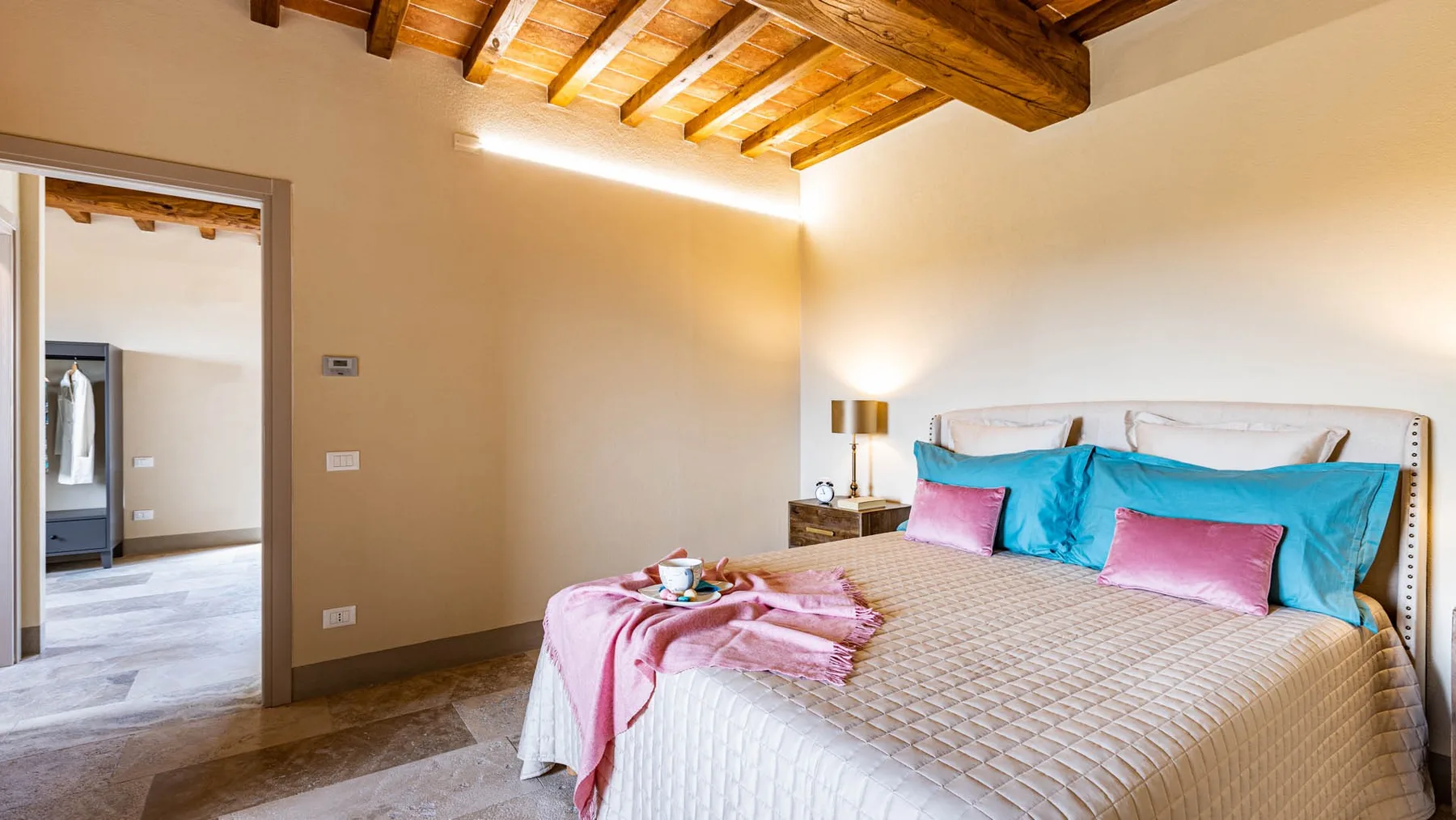 A bedroom with a large bed, colorful pillows, and exposed wooden ceiling beams.
