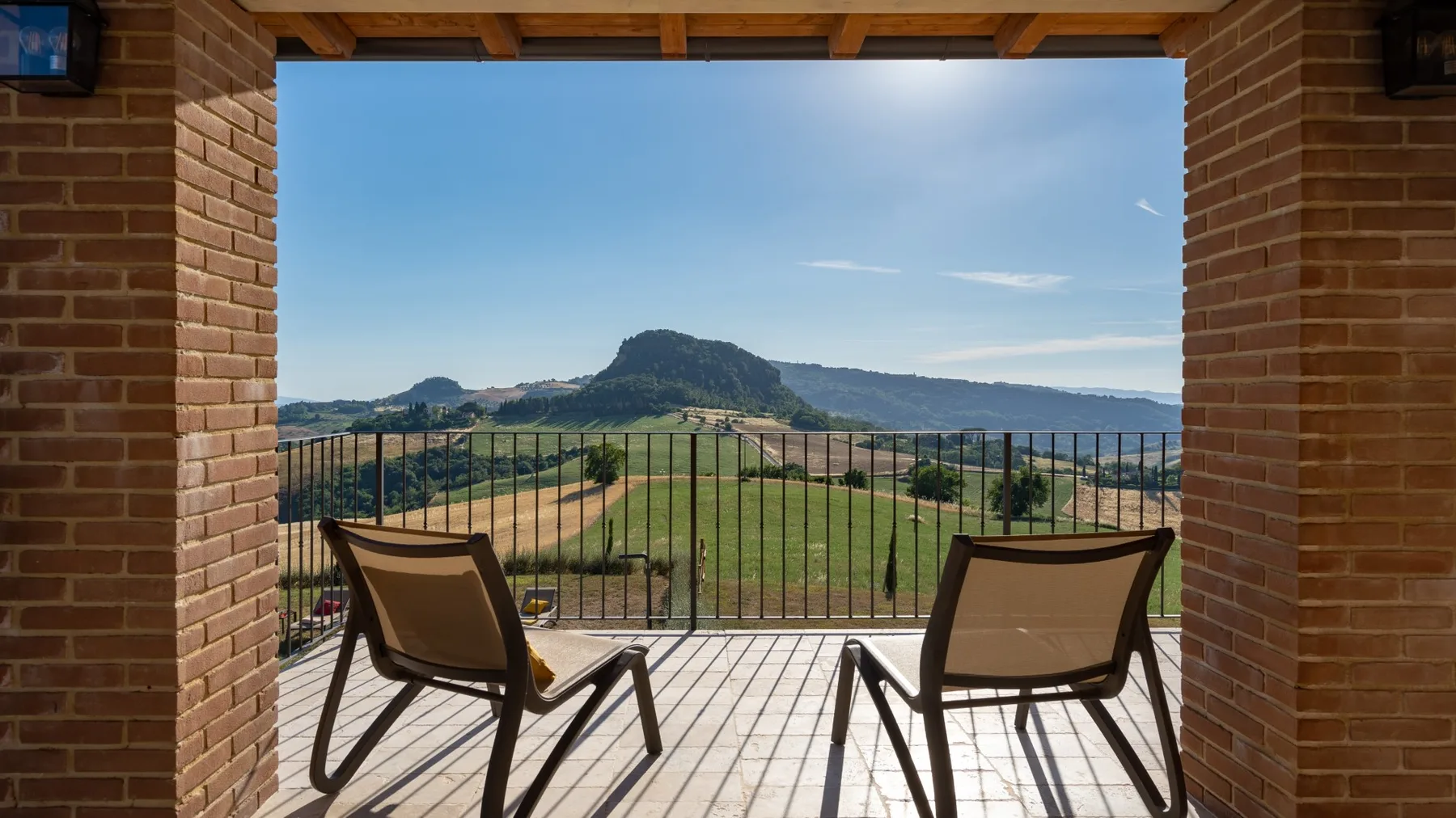 A covered balcony overlooks green hills and a distant mountain.