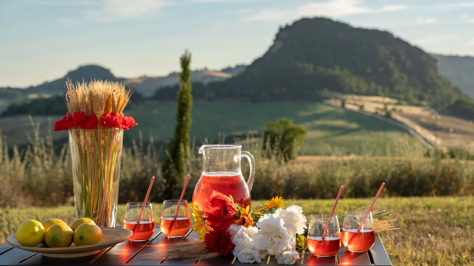 A table with drinks and flowers overlooks a green, hilly landscape.