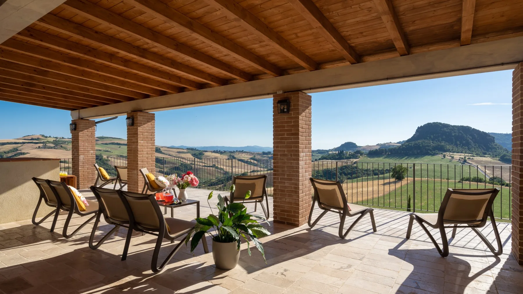 A covered terrace has seating and open views across a hilly landscape.