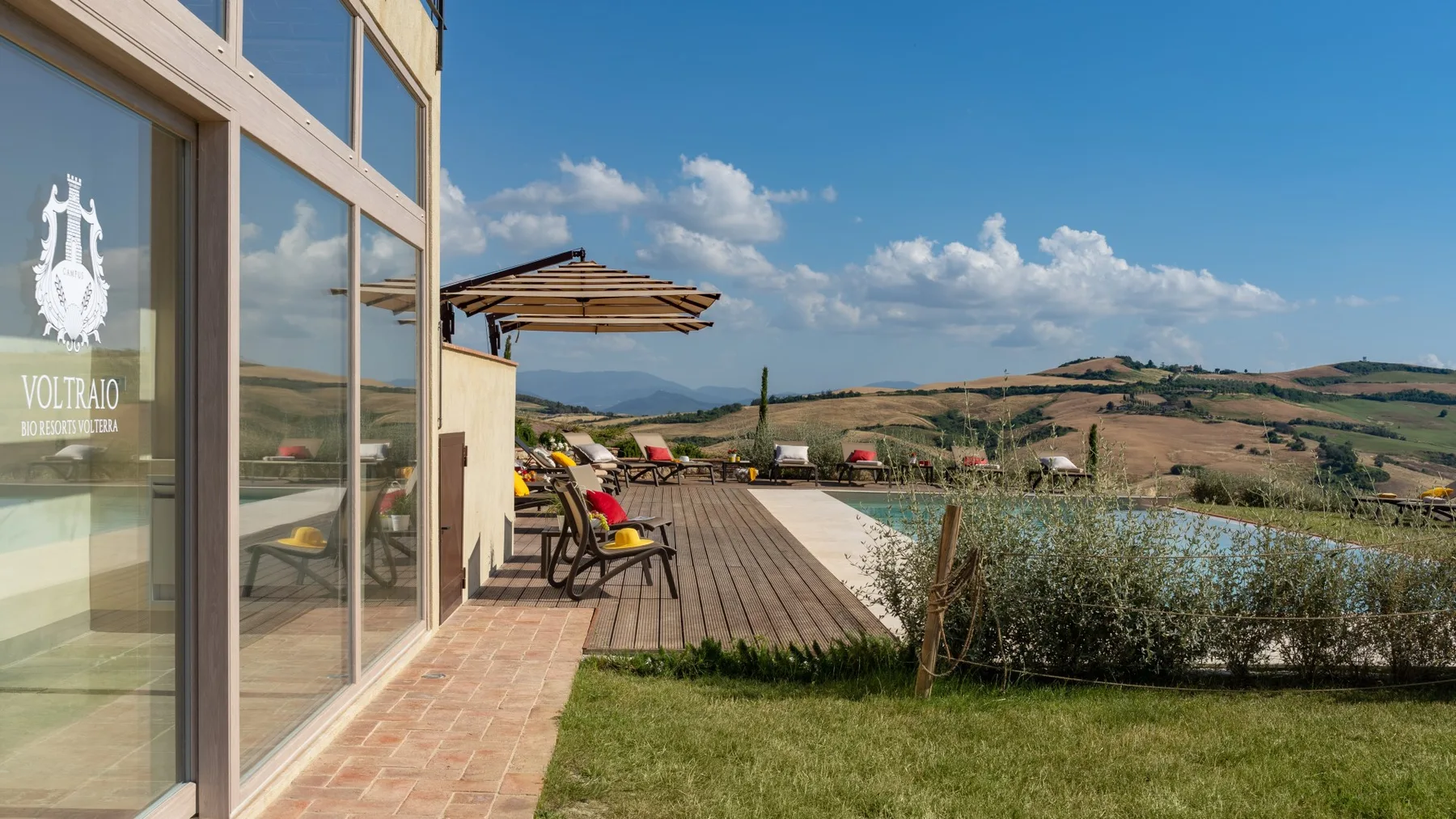 A sunny outdoor terrace with seating and umbrellas overlooks rolling hills.